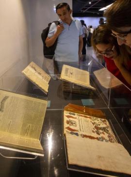 3 personas viendo unos libros abiertos que están dentro de una vitrina 