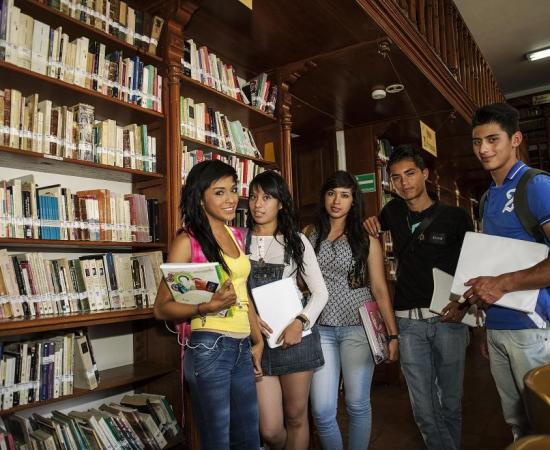 5 personas paras en un estante de libros y cada unos de ellos tiene un libro en la mano