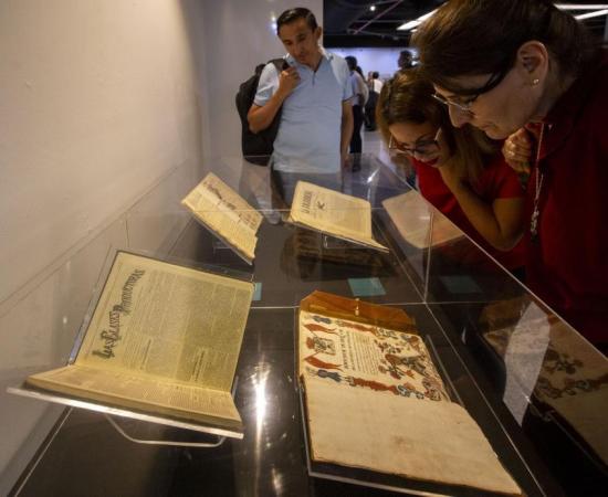 3 personas viendo unos libros abiertos que están dentro de una vitrina 